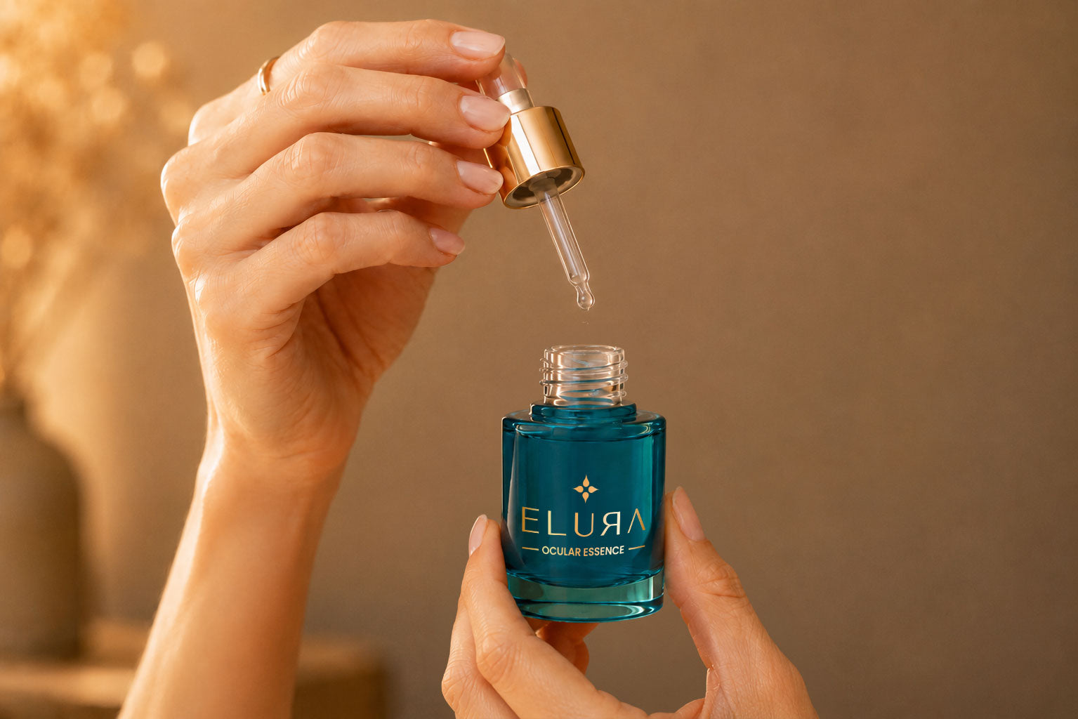 A person holds a dropper above an open blue bottle labeled ELURA Celluar Essence, ready to dispense a liquid. The background is softly lit and neutral.